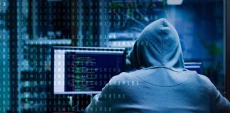 Person in hoodie working at computer with code on screens