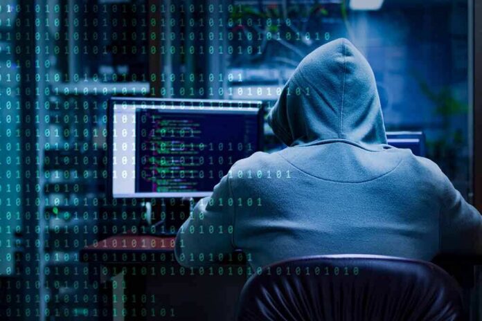 Person in hoodie working at computer with code on screens