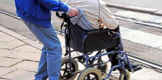 Caregiver pushing person in wheelchair over curb