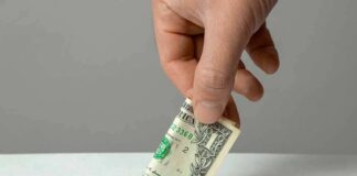Hand inserting a folded dollar bill into a small slot