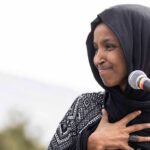 Woman in black hijab speaking at a microphone outdoors