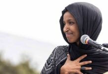 Woman in black hijab speaking at a microphone outdoors