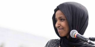 Woman in black hijab speaking at a microphone outdoors