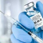 Gloved hands holding a vaccine vial and syringe