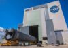 Rocket stage moved on transporter outside large NASA assembly building