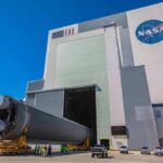 Rocket stage moved on transporter outside large NASA assembly building