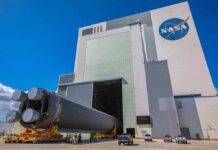 Rocket stage moved on transporter outside large NASA assembly building
