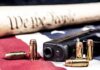 Quiet DOJ Move Rattles Gun Debate Handgun with bullets on American flag near parchment