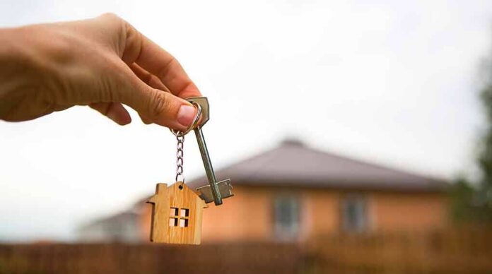 shutterstock_1920801920 Hand holding house key with wooden house keychain