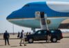Security detail near blue and white aircraft with staircase and SUV