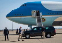 Security detail near blue and white aircraft with staircase and SUV