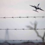Airplane taking off above barbed wire fence