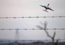 U.S. Deportation Puts Ex-Minister On Trial Airplane taking off above barbed wire fence