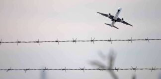 Airplane taking off above barbed wire fence