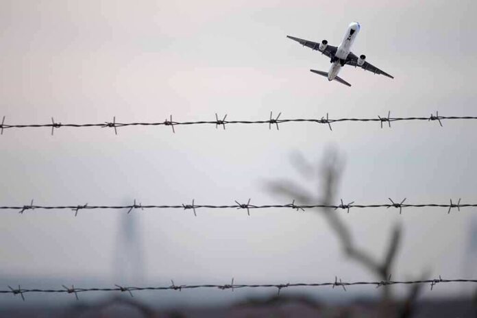 shutterstock_2401451327 Airplane taking off above barbed wire fence