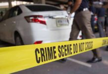 Yellow crime scene tape in front of a white car with investigators nearby