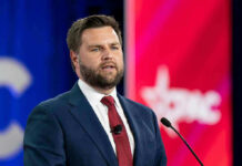 Vance Drops Fraud Hammer – Who Gets Cut? Man in suit speaking at a podium with microphone