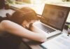 Michigan’s New Grade Policy Sparks Debate Woman resting her head on desk beside an open laptop