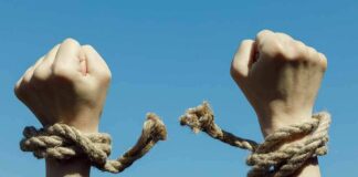 Hands breaking free from rope bindings against a clear blue sky