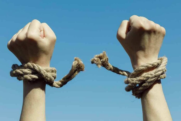 shutterstock_1082949368 Hands breaking free from rope bindings against a clear blue sky