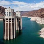 Record Low Threatens Southwest Power A large dam structure with two towers over a blue water reservoir surrounded by rocky mountains