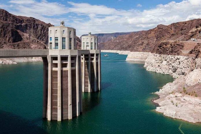 shutterstock_110290532 A large dam structure with two towers over a blue water reservoir surrounded by rocky mountains