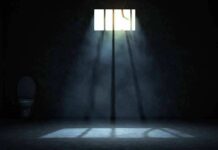 Empty prison cell with light beams through a small barred window
