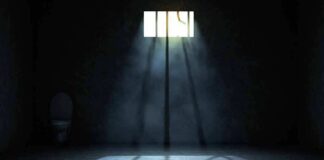Empty prison cell with light beams through a small barred window