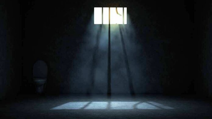 Empty prison cell with light beams through a small barred window