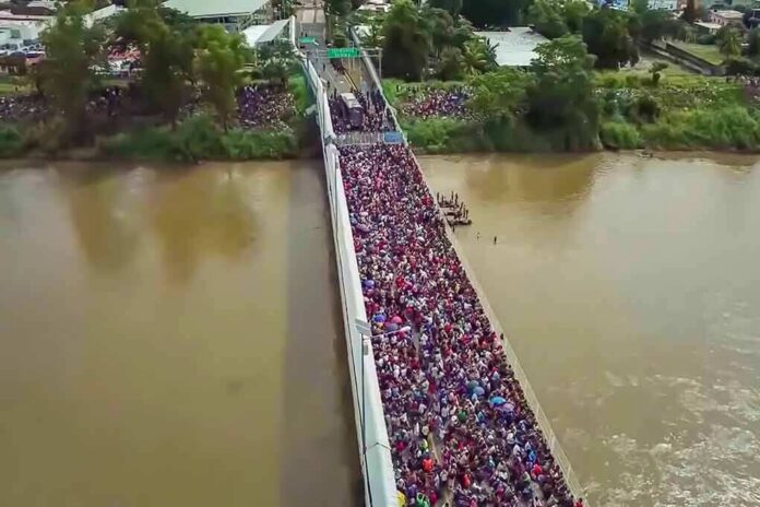 shutterstock_1229072224 Crowd of people densely packed on a bridge over a muddy river