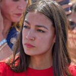 Why AOC ‘Lied’ Story Keeps Returning woman in red top at an outdoor event