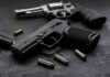 Handgun and revolver with scattered bullets on dark surface