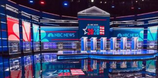 Televised debate stage with multiple podiums and bright red, white, and blue lighting