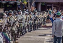 FBI Steps In After ICE Gunfire Riot police in helmets and shields form a line on a city street
