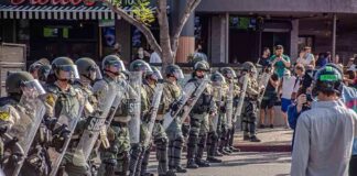 Riot police in helmets and shields form a line on a city street