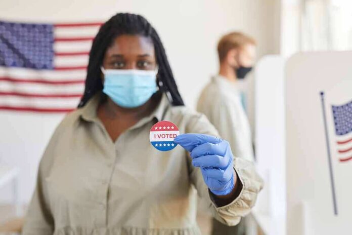 Voter wearing a mask holds an I Voted sticker at a polling place