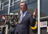 Gavin Newsom speaks at a press conference with microphones outside a building