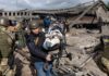 Rescuers carry a baby in a stroller through a destroyed bridge