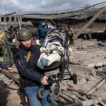 Ambulance Targeted After Suicide Bomb Rescuers carry a baby in a stroller through a destroyed bridge