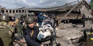 Rescuers carry a baby in a stroller through a destroyed bridge