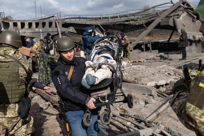 Rescuers carry a baby in a stroller through a destroyed bridge