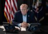 Trump Blasts Bail After Base Scare Donald Trump seated at a table between two desk phones