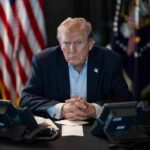 Trump Blasts Bail After Base Scare Donald Trump seated at a table between two desk phones