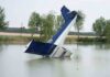 An abandoned aircraft partially submerged in a calm body of water surrounded by trees