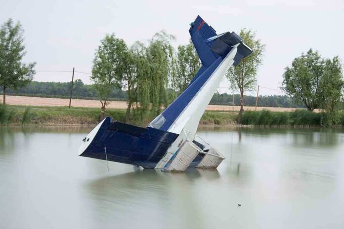 An abandoned aircraft partially submerged in a calm body of water surrounded by trees