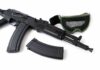 Black rifle with magazine and green mesh goggles on white background