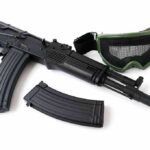Congress Targets BB Guns Next? Black rifle with magazine and green mesh goggles on white background
