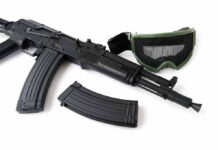 Black rifle with magazine and green mesh goggles on white background