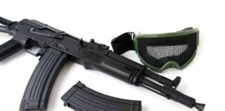 Black rifle with magazine and green mesh goggles on white background