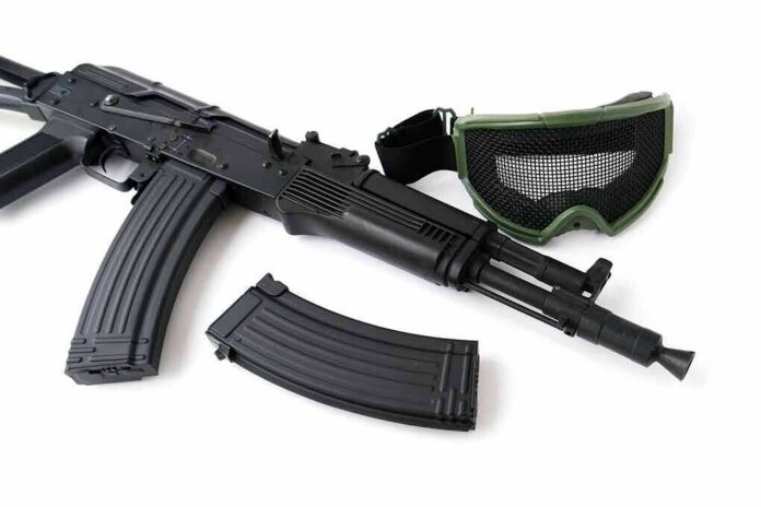 shutterstock_480755515 Black rifle with magazine and green mesh goggles on white background